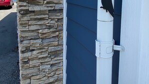 A bird perched on a white gutter attached to a building with a stone facade. - Raven’s Nest – Cozy Lower One‑Bedroom Suite (Victoria)