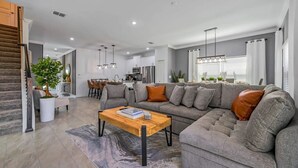 A modern living room with a grey sectional sofa, a wooden coffee table, and a dining area in the background. - Themed Home w/ Pool at Storey Lake (kissimmee)