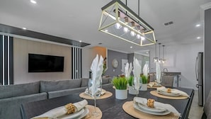 A modern dining area with a long table set for four, a sofa, and a kitchen in the background. - Themed Home w/ Pool at Storey Lake (kissimmee)