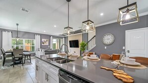 A modern kitchen with a large island, pendant lights, and a dining area with a view of the outdoors. - Themed Home w/ Pool at Storey Lake (kissimmee)