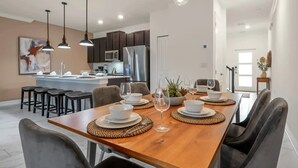 Una cocina moderna con armarios oscuros, una isla central y una zona de comedor con una mesa de madera para cuatro.