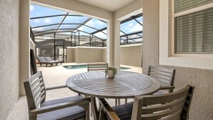 Un espacio al aire libre cubierto con una mesa redonda y sillas, una piscina y sillones de descanso.