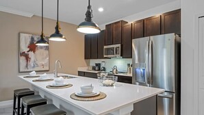 Una cocina moderna con una isla central, electrodomésticos de acero inoxidable, armarios de madera oscura e iluminación colgante.