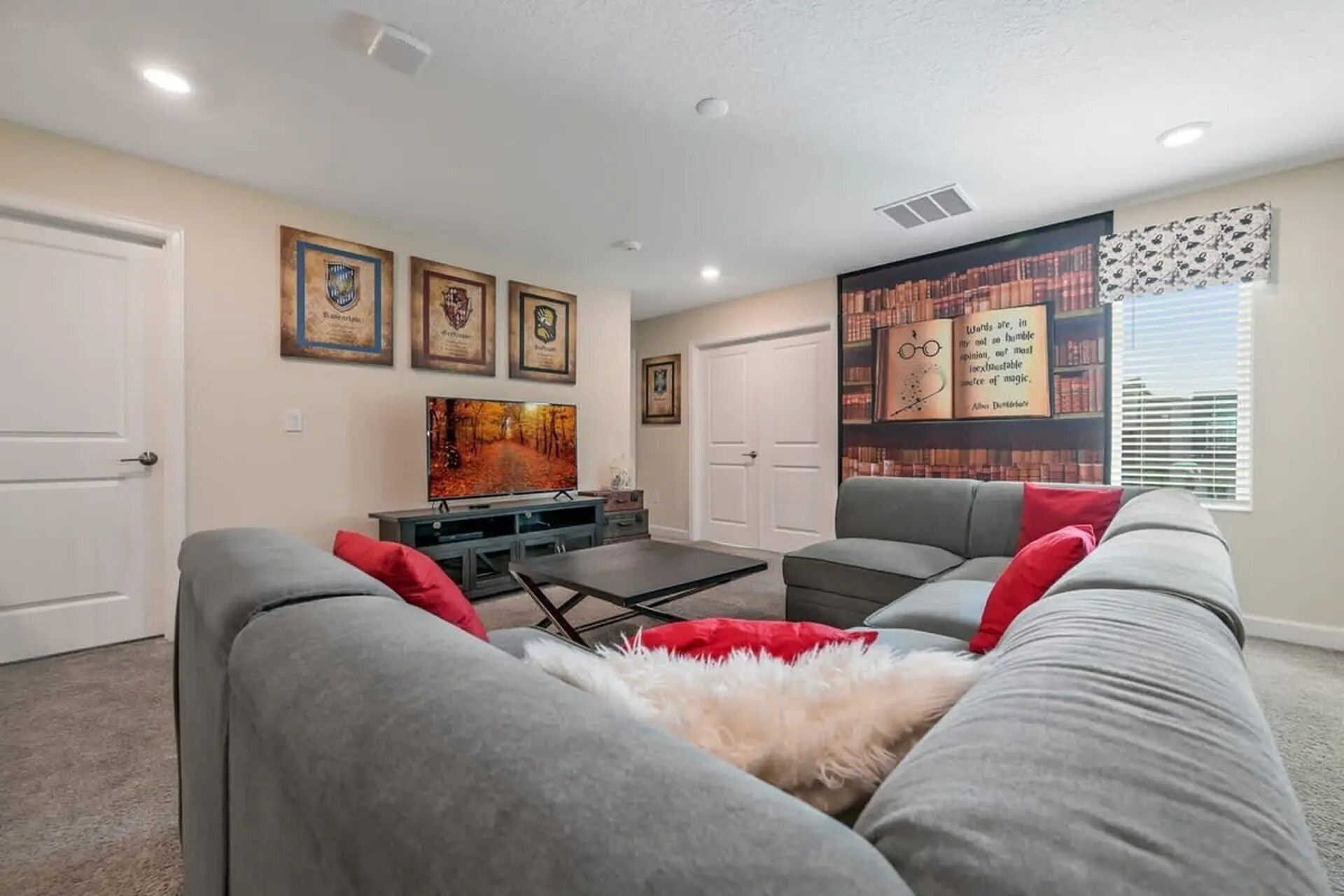 A living room with grey sofas, a flat-screen TV, framed certificates on the wall, and a bookshelf with books and a quote poster.