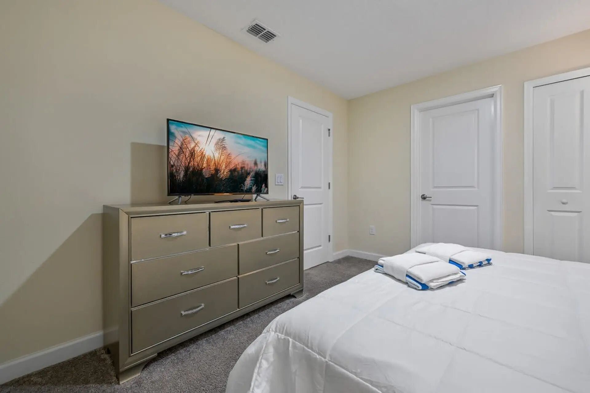 A bedroom with a bed, a television on a dresser, and two doors.
