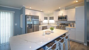 A modern kitchen with white cabinets, stainless steel appliances, and a marble island with bar stools. - Ocean Breeze 2BR/2BA Beach Getaway (Fort Myers Beach)