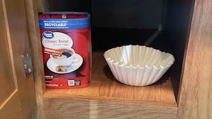 A cabinet with a box of Great Value Classic Roast Ground Coffee and a white ceramic bowl.