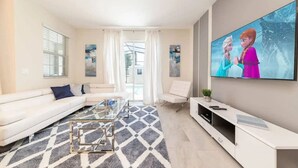 A modern living room with a sofa, coffee table, and a flat-screen TV displaying animated characters. - Home w/ Private Pool 10 min to Disney (Kissimmee)