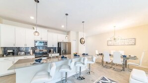 A modern kitchen with white cabinets, stainless steel appliances, and a central island with bar stools. - Home w/ Private Pool 10 min to Disney (Kissimmee)