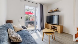 Una sala de estar moderna con un sofá, un televisor sobre un mueble de madera y un ventanal corredero que da a un espacio exterior.