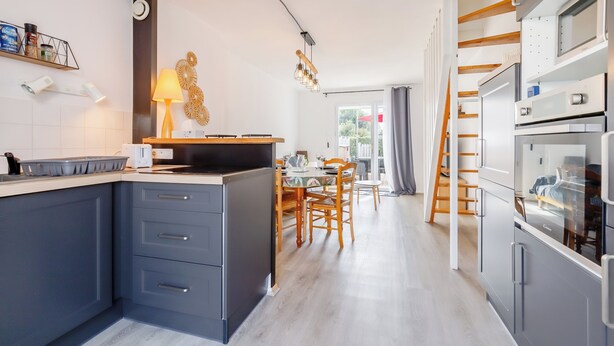 Una cocina moderna con armarios grises, una isla central y un comedor con sillas y mesa de madera.