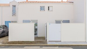 Un edificio blanco con techo de tejas, un coche estacionado en la entrada y un pequeño portón.