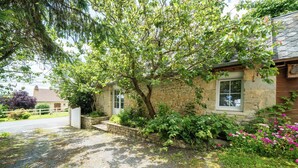 Ein Steinhaus mit Kiesweg, Holzzaun und einem Garten mit verschiedenen Pflanzen und Blumen.