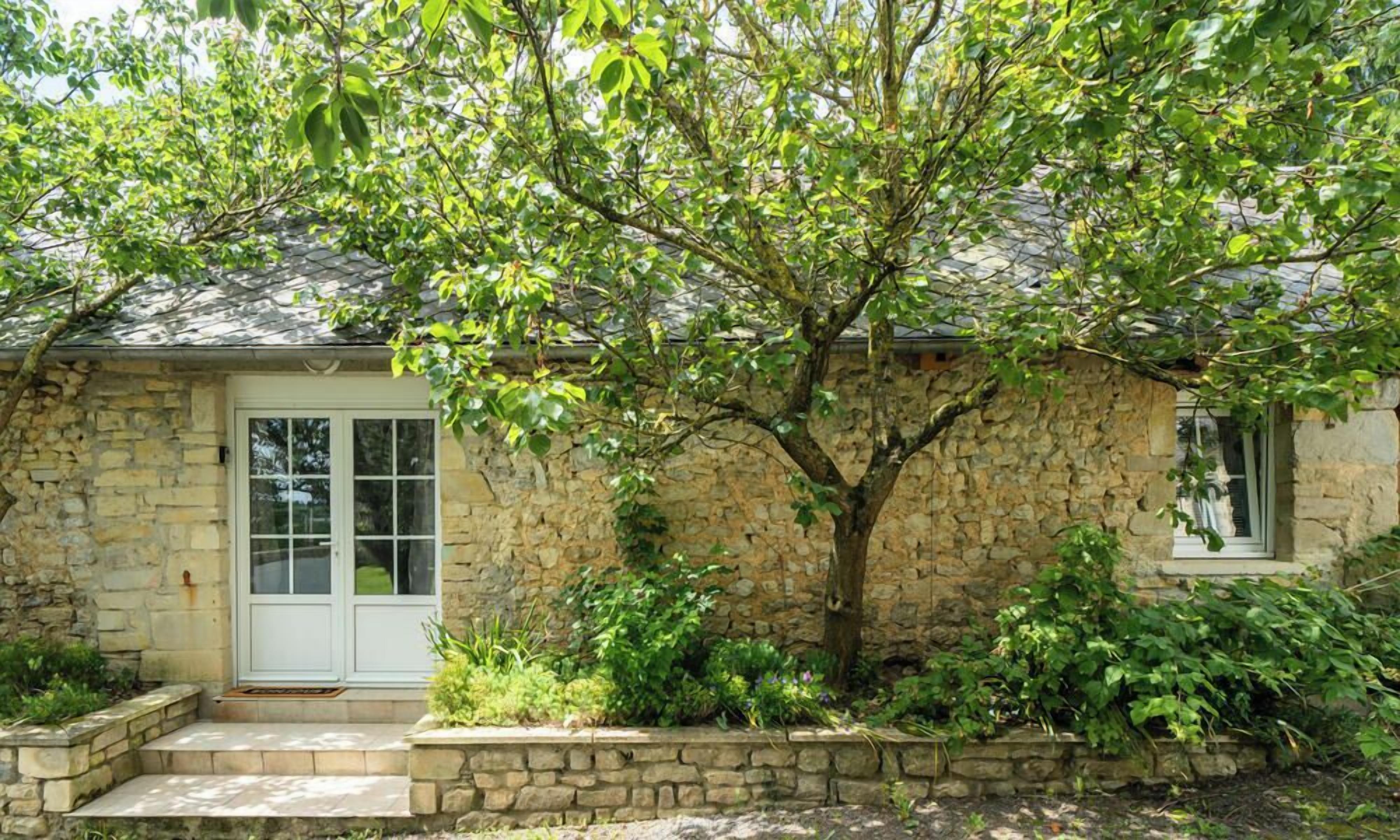 A stone house with a white door, a small porch, and a tree in front.
