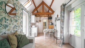Ein gemütliches Wohnzimmer mit einer Couch, einem Essbereich mit Tisch und Stühlen, einer Küche mit Kühlschrank und einer Uhr sowie einem Fenster mit Vorhängen.