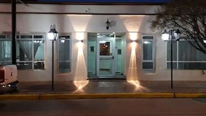 A building with a glass door entrance, two street lamps, and a vehicle parked in front. - Hotel Mora (Puerto Madryn)