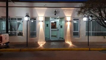 Un edificio con puerta de acceso de vidrio, dos farolas y un vehículo estacionado adelante.