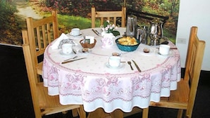 A round dining table with a white tablecloth and pink floral pattern, surrounded by wooden chairs. - Hotel Mora (Puerto Madryn)