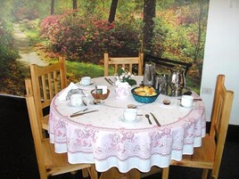 Una mesa redonda para comer con mantel blanco y estampado floral rosa, rodeada de sillas de madera.