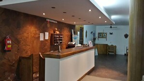A reception area with a stone wall, wooden reception desk, and a fire extinguisher. - Hotel Mora (Puerto Madryn)
