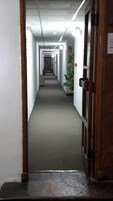Un pasillo largo y estrecho con piso alfombrado, paredes blancas y una puerta al final.