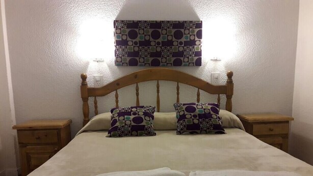 A bed with a wooden headboard, two nightstands, and two pillows with a geometric pattern. There are two folded white towels on the bed. - Hotel Mora (Puerto Madryn)