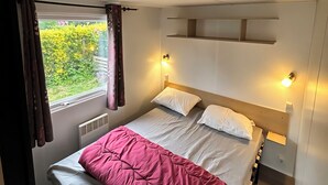 Une chambre à coucher avec un lit, une fenêtre avec des rideaux, un radiateur et des lampes fixées au mur.