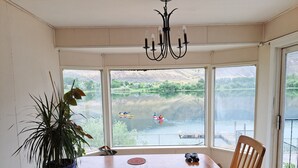 A dining area with a large window overlooking a calm lake and kayakers. - Private Room at Riverfront House (Kamloops)
