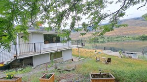 Una casa amb terrassa que domina un llac, envoltada de vegetació i un paisatge amb turons.