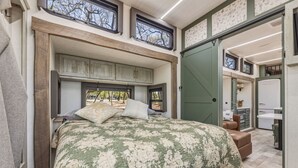 A bedroom with a bed, a window, a door, and a small kitchenette. - Private Lakeside RV Escape with Hot Tub, Multi-Level Deck, & Easy Water Access (Corsicana)