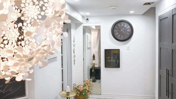 A hallway with a large wall clock, a framed quote, and a decorative plant. - Ivy Den (Oakville)