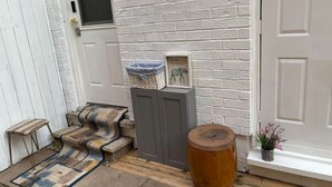 A front door with a white picket fence, a small porch with a rug, a wicker basket, and a wooden stool. - Ivy Den (Oakville)
