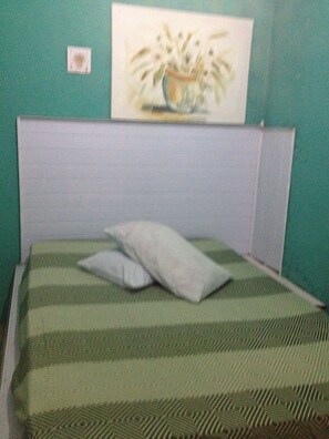 A room with a bed featuring a green and white striped bedspread, a pillow, and a headboard against a teal wall. - Pousada Morada da Praia (São Vicente)