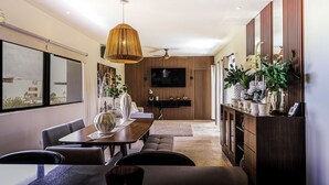 A modern living room with a dining area, a flat-screen TV mounted on a wooden wall, a ceiling fan, and a large window with a view of buildings. - Palmares (Playa del Carmen)