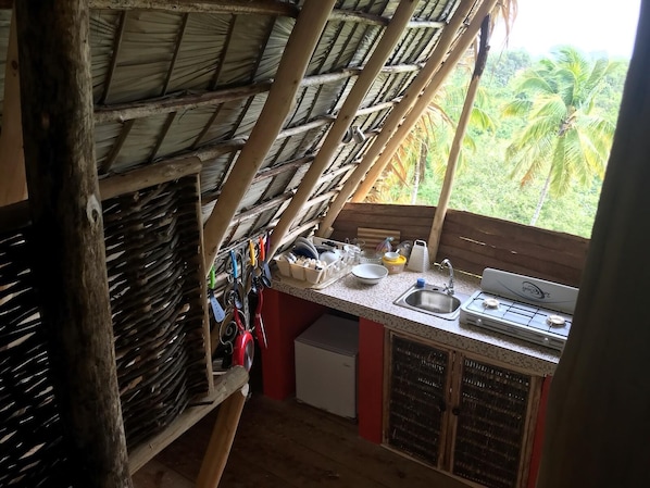A compact kitchen with a thatched roof, a sink, a stove, and various kitchen utensils. - Eco Casa Algana (Samaná)