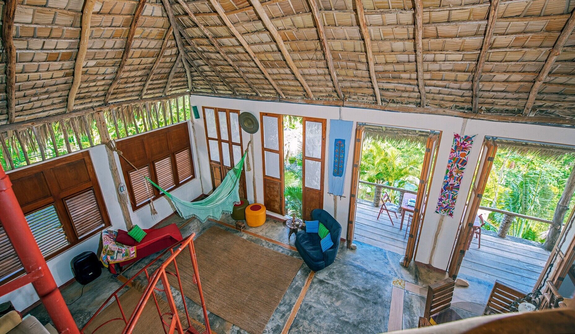 A room with a thatched roof, wooden furniture, a hammock, and a view of greenery outside.