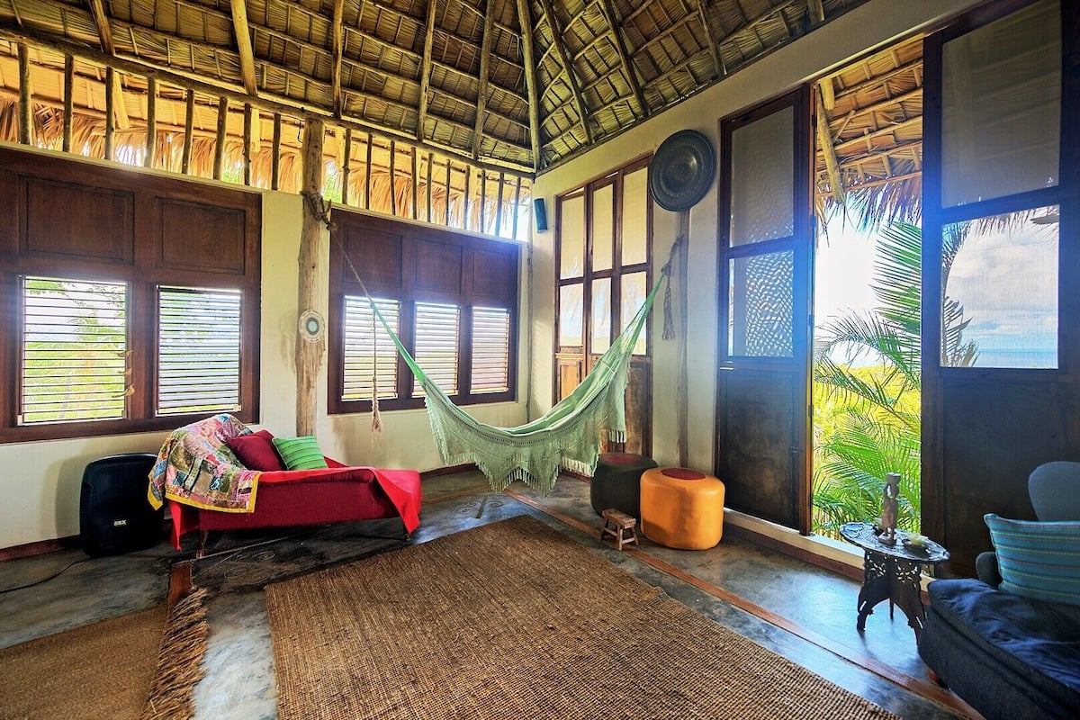A room with a hammock, a red sofa, and a view of greenery outside.