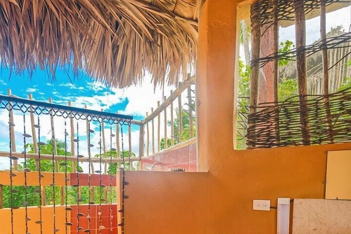 A bathroom with a thatched roof, a toilet, a sink, and a window with a view of greenery.