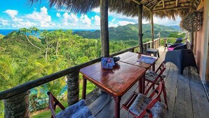 Une terrasse en bois avec une table et des chaises, offrant une vue imprenable sur un paysage luxuriant et l’océan.