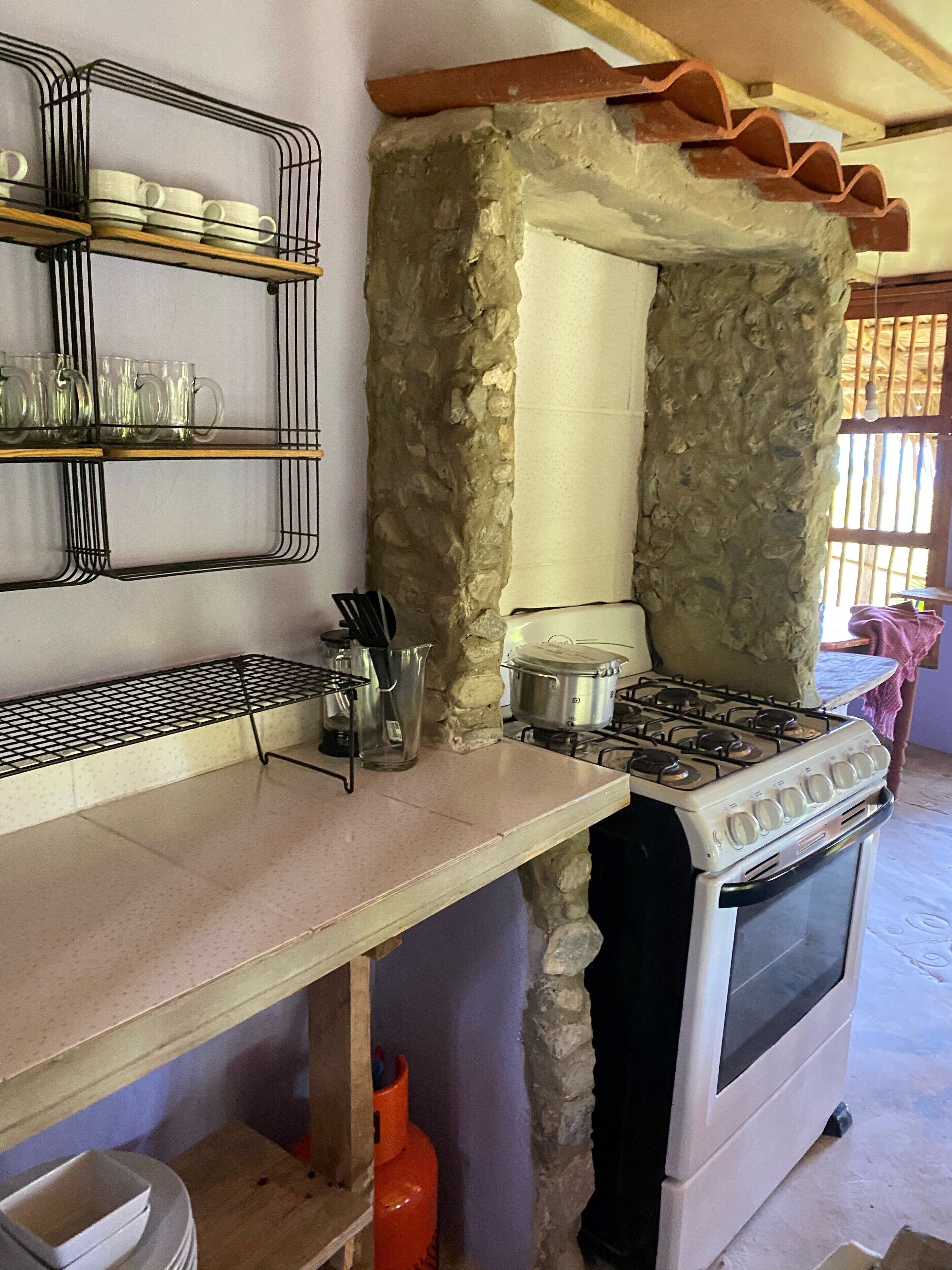 A kitchen with a stone wall, a gas stove, and a sink.