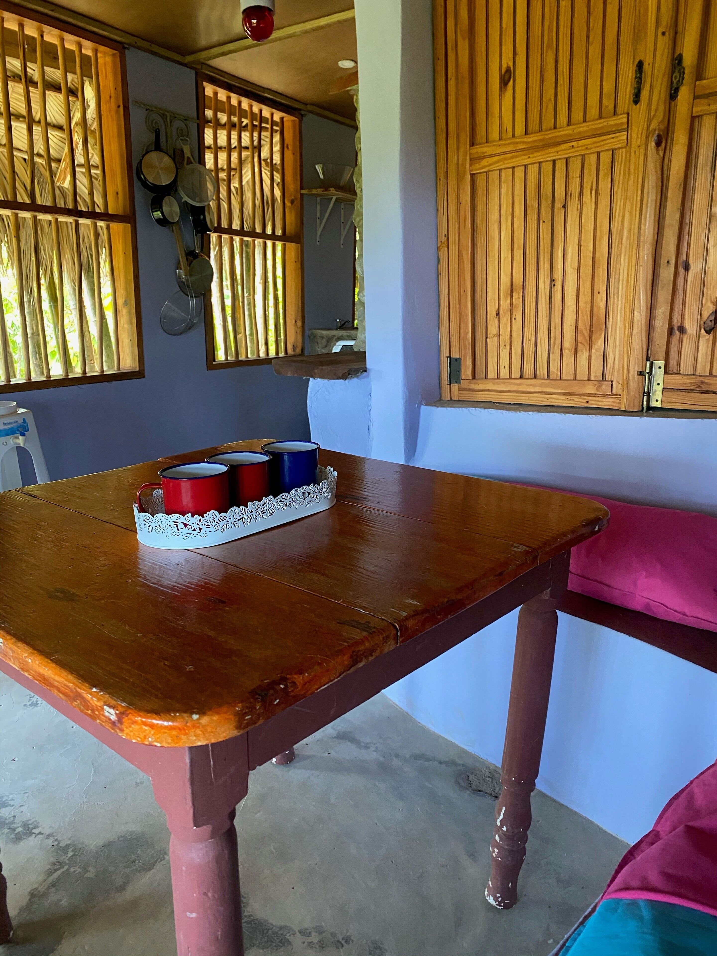 A wooden table with a lace table runner and a tray of red, blue, and white cups.