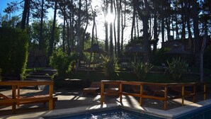 A pool area with wooden deck and lounge chairs, surrounded by trees and umbrellas. - Alamos Hosteria (Mar Azul)
