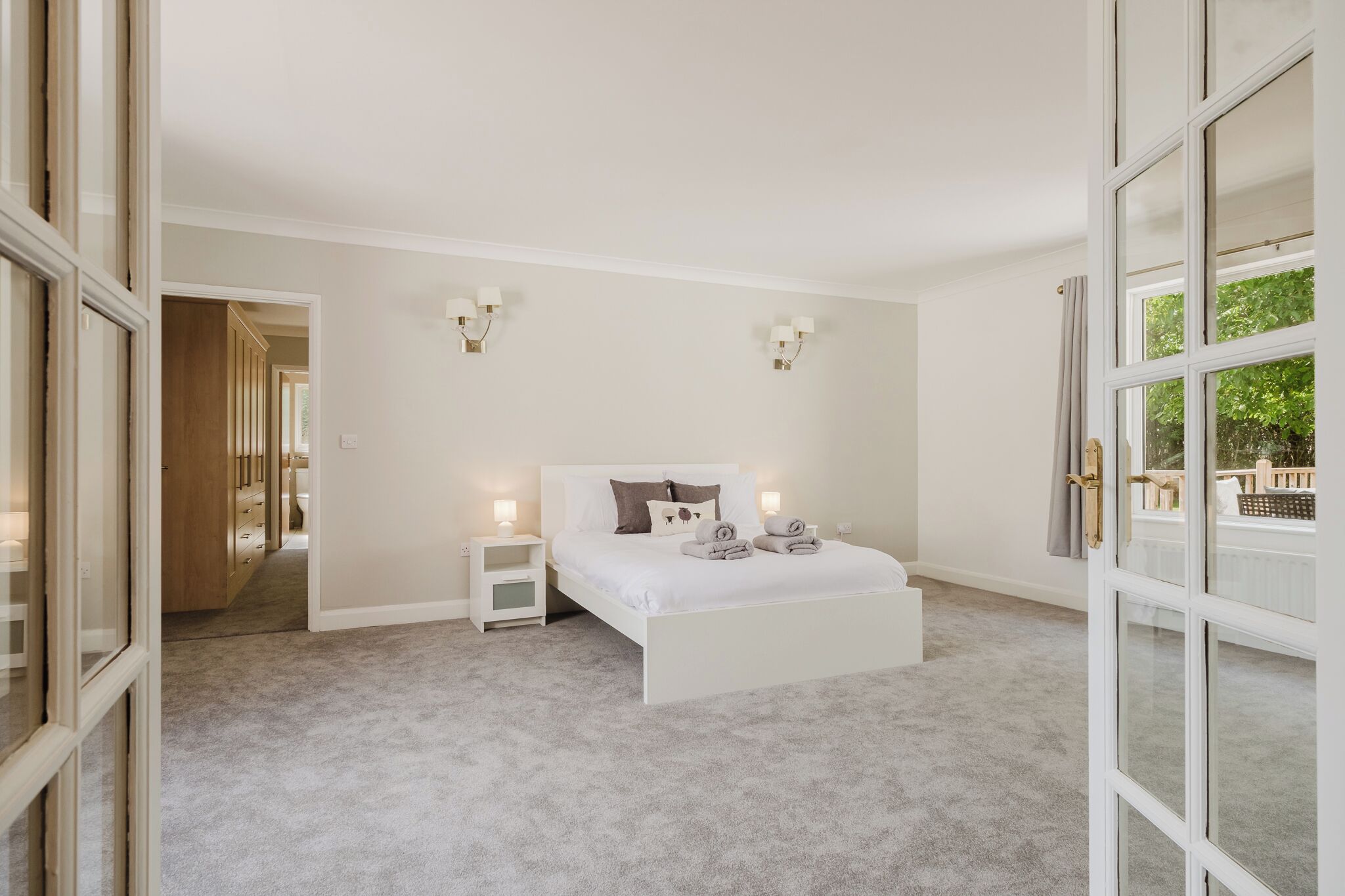 A bedroom with a large bed, bedside tables, and a view of a balcony.