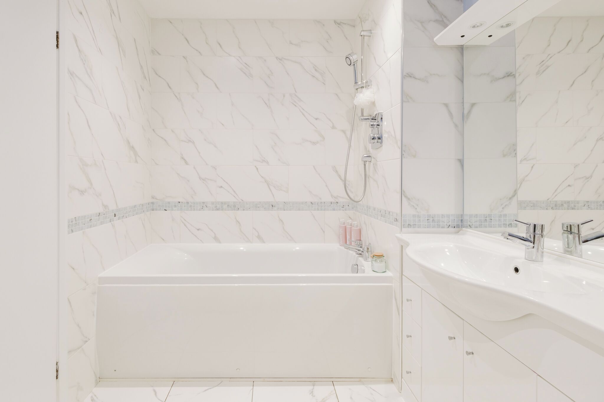 Un bagno moderno con una parete in marmo, una vasca freestanding, un ampio lavabo con specchio e un soffione doccia.