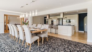 Uma sala de jantar moderna com mesa e cadeiras de madeira, um tapete estampado e iluminação pendente.