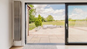 Interior moderno de uma casa com uma porta de correr de vidro que dá para um pátio com mobiliário exterior e vista para uma paisagem verde.