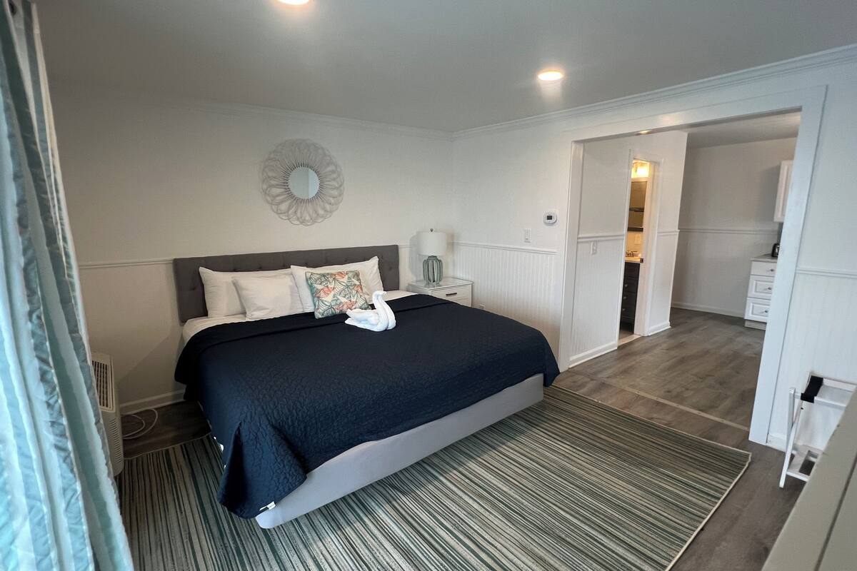 A neatly arranged bedroom with a bed, bedside table, and a mirror on the wall.