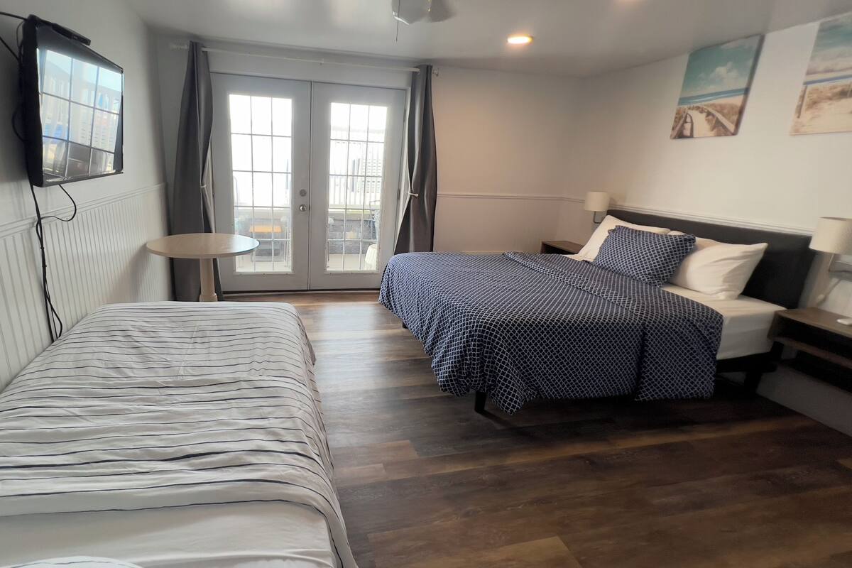 A hotel room with a bed, a desk, a chair, a TV, and a window with curtains.
