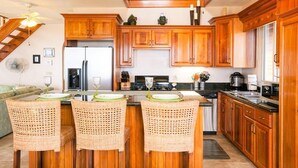 Eine Küche mit Holzausstattung, einem Kühlschrank, einem Essbereich mit Korbstühlen und einer Treppe.