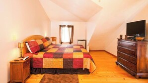 Ein Schlafzimmer mit kariertem Bettbezug, einem hölzernen Schminktisch und einem Fernseher auf einem Schrank.
